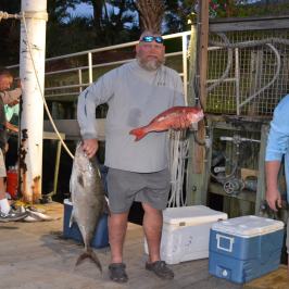a group of people standing next to a man holding a fish