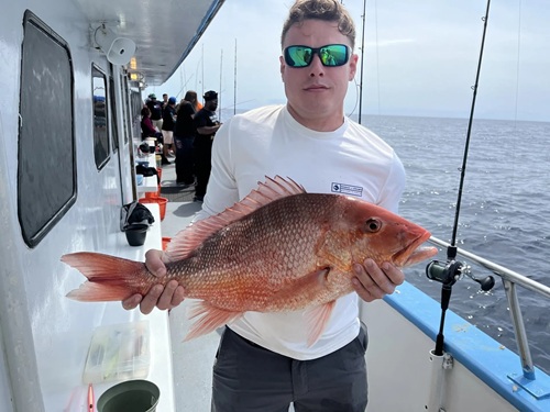 deep sea fishing in Myrtle Beach SC Person holding a large red fish on a boat with fishing rods and ocean in background.