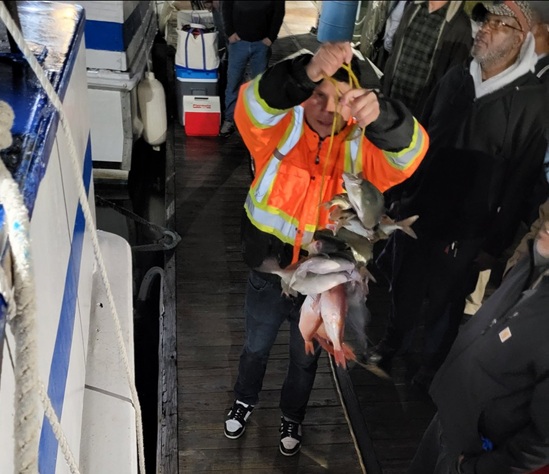 Person in orange jacket holding several fish on a dock with others nearby.