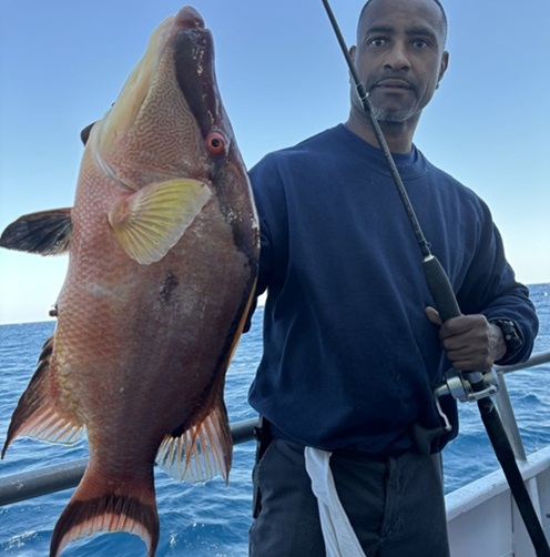 Person holding a large fish on a boat with a fishing rod.