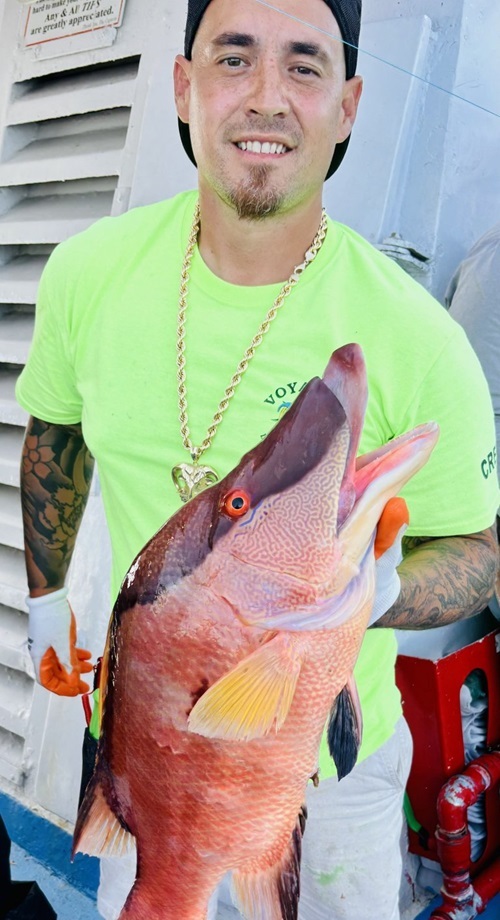 Man in a bright shirt holding a large fish on a boat.