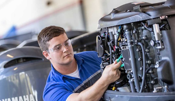 Man in blue shirt working on a boat engine, wearing safety glasses.
