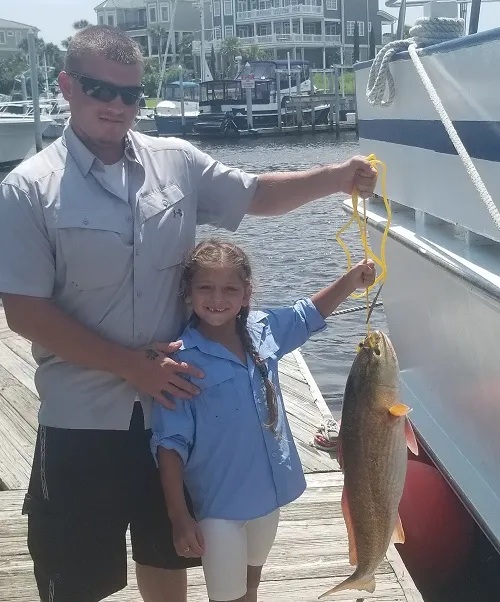 Deep sea fishing in Myrtle Beach SC Man and girl holding a large fish on a dock next to a boat.