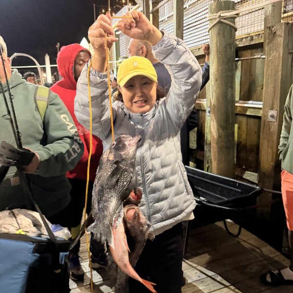 Person holding fish on a dock at night, surrounded by onlookers.