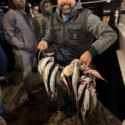 Smiling man on boat holding a string of fish at night, surrounded by others.
