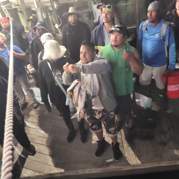 Group of people on a wooden dock, some wearing hats and holding fish.