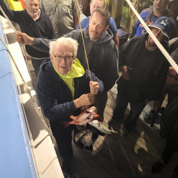 Group on a boat, one person holding a caught fish, others watching.