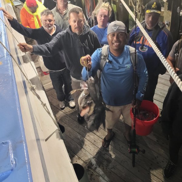 Group of people on a dock, one holding a fish and fishing rod, others standing around smiling.