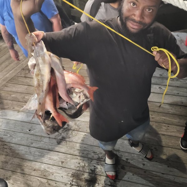 Man holding several fish on a yellow string, standing on a wooden deck.
