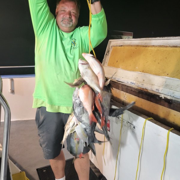Man holding a line with multiple fish on a boat deck.