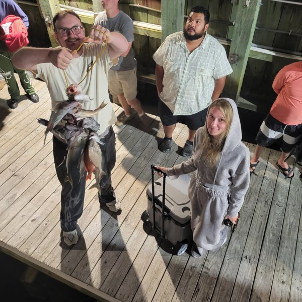 People on dock, man holding fish, others watching, night.
