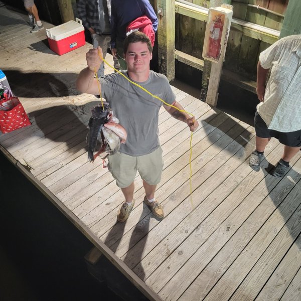 Man on dock holding fish, with two other people nearby.
