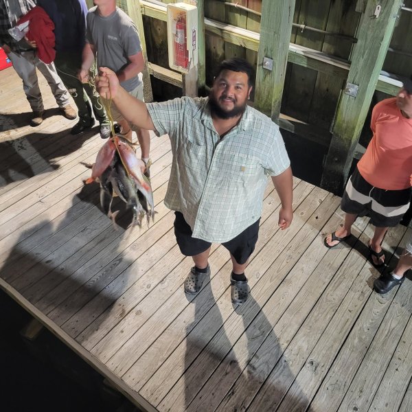 Man holding fish on a dock with others nearby, nighttime setting.
