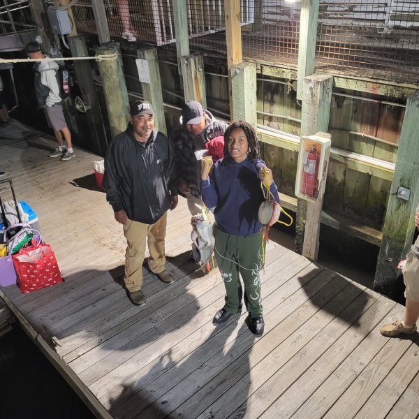 People on a wooden dock holding fish at night with gear around.