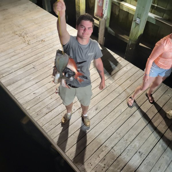 Man on dock holding fish with others nearby.