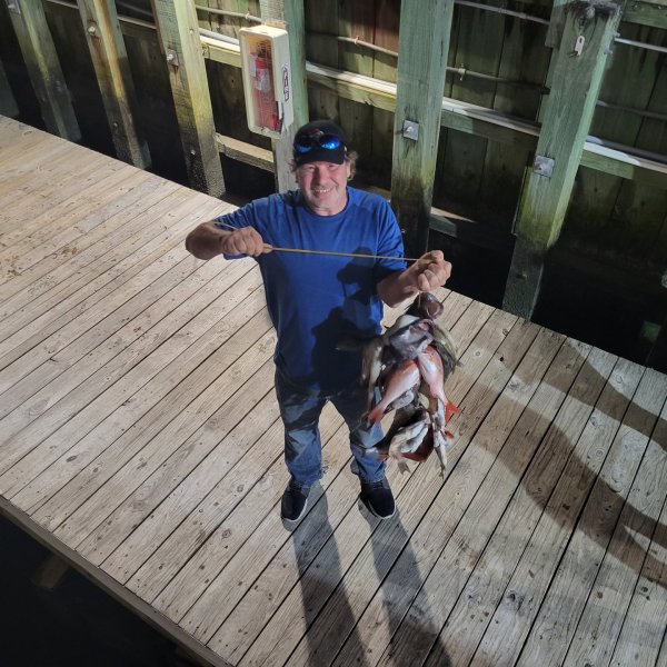 Man holding several fish on a wooden dock, smiling at the camera.